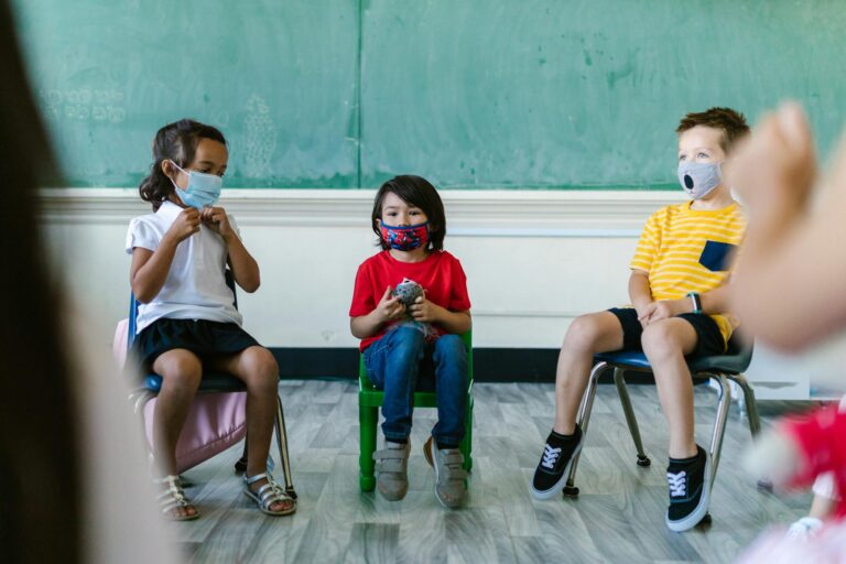 Children wearing masks sitting in a classroom setting, focused and engaged.